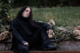 Portrait eines Mannes mit langen Haaren, der sitzt und ein Bein auf der Bank hat, fotografiert von LiraAmarokPictures