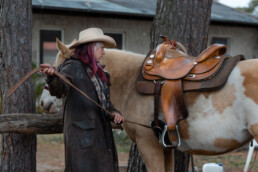 Beige Painthorsestute mit Stephanie Richter beim Satteln, Gurt festziehend, fotografiert von LiraAmarokPictures