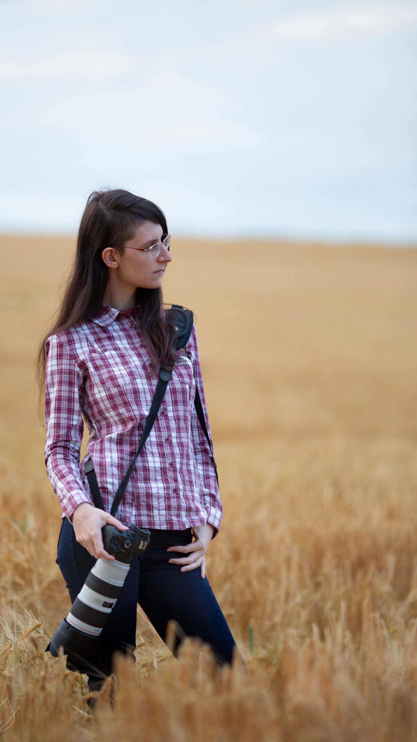 Fotografin mit rotem Karohemd und Kamera an der Seite steht in einem Getreidefeld