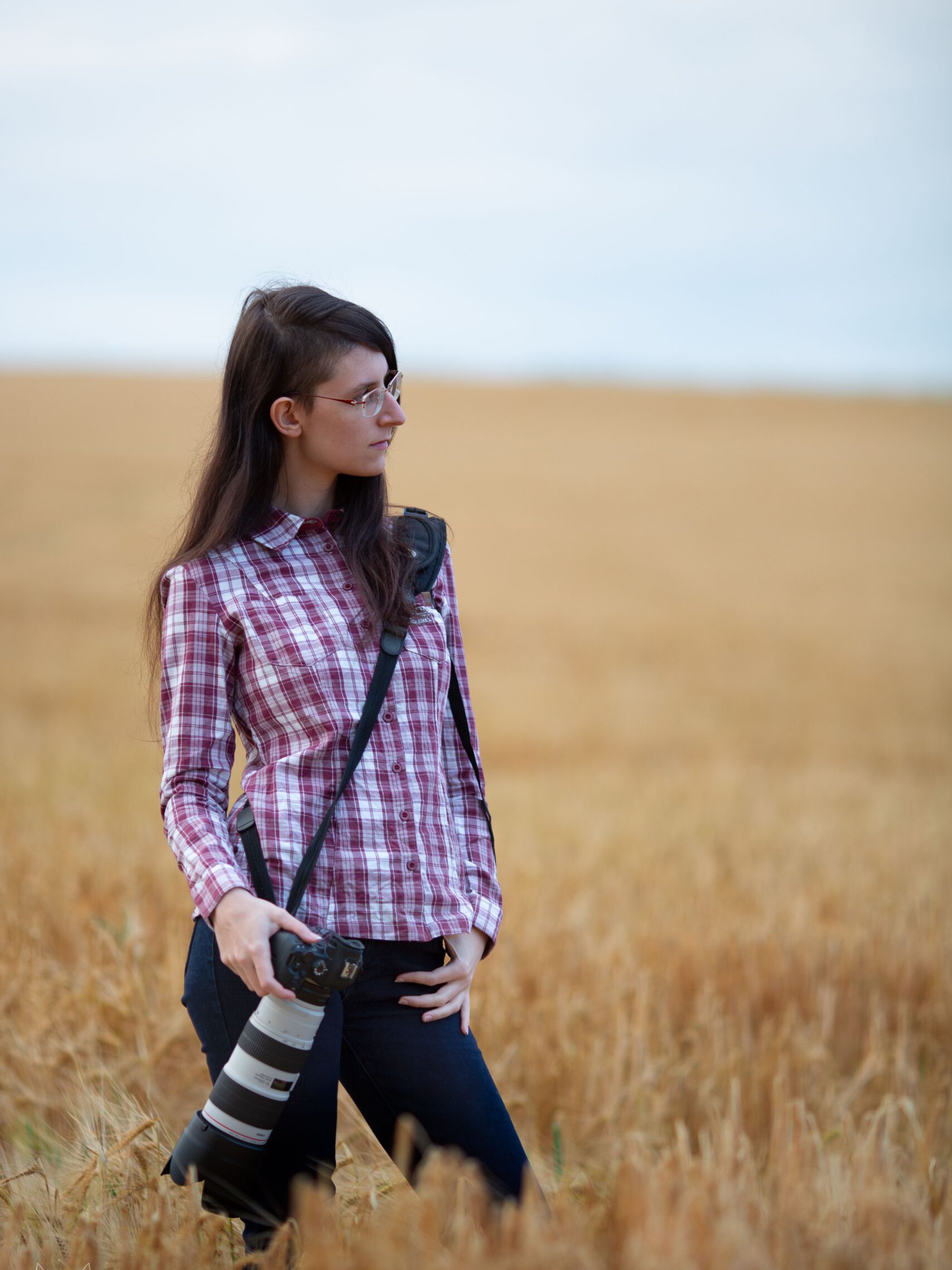 Fotografin mit rotem Karohemd und Kamera an der Seite steht in einem Getreidefeld