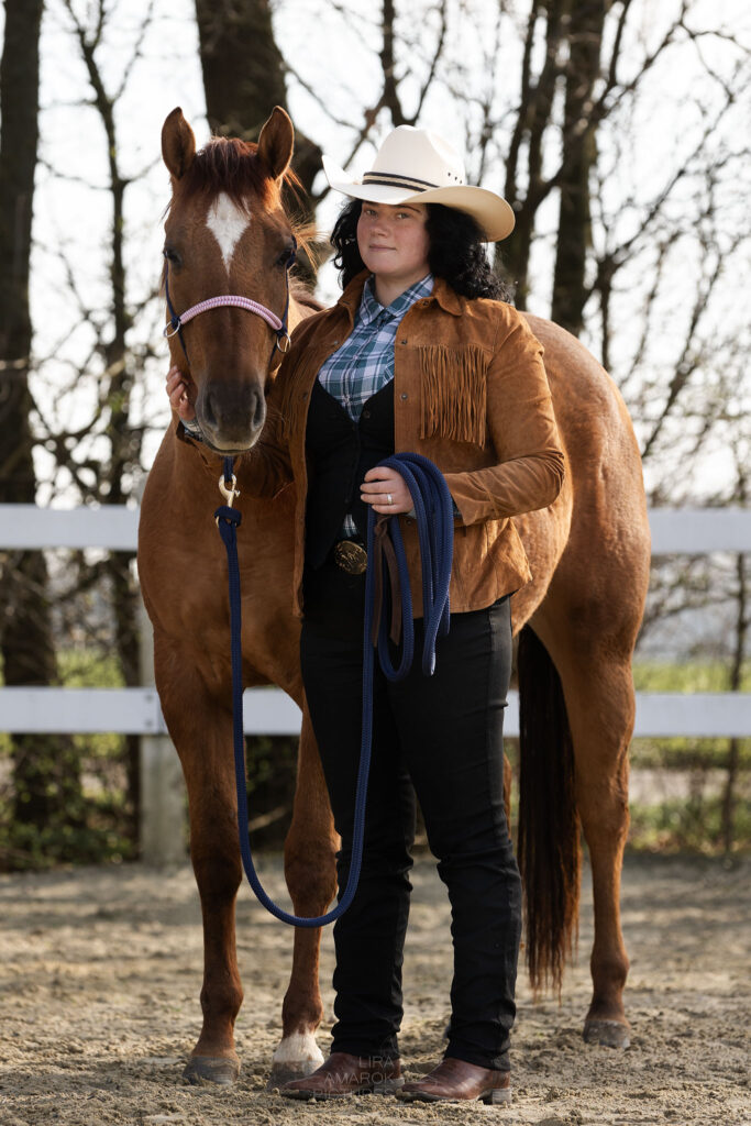 Porträt einer Westernreiterin neben ihrem Pferd, dass ein Knotenhalfter trägt