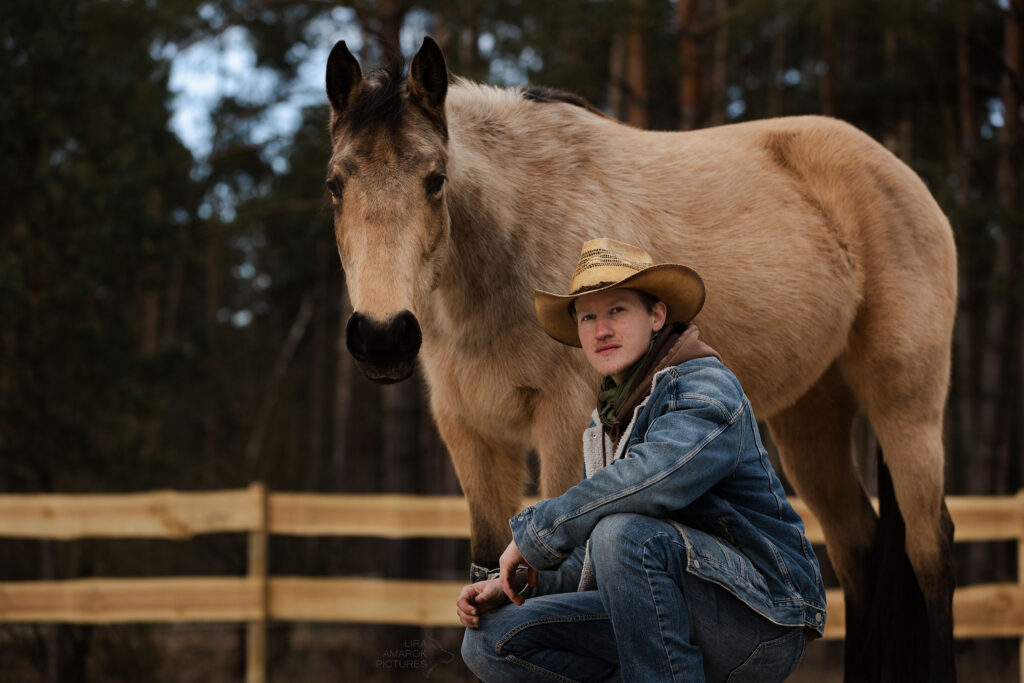 Besitzer und Pferd schauen in die Kamera. Mensch kniet, Pferd steht dahinter