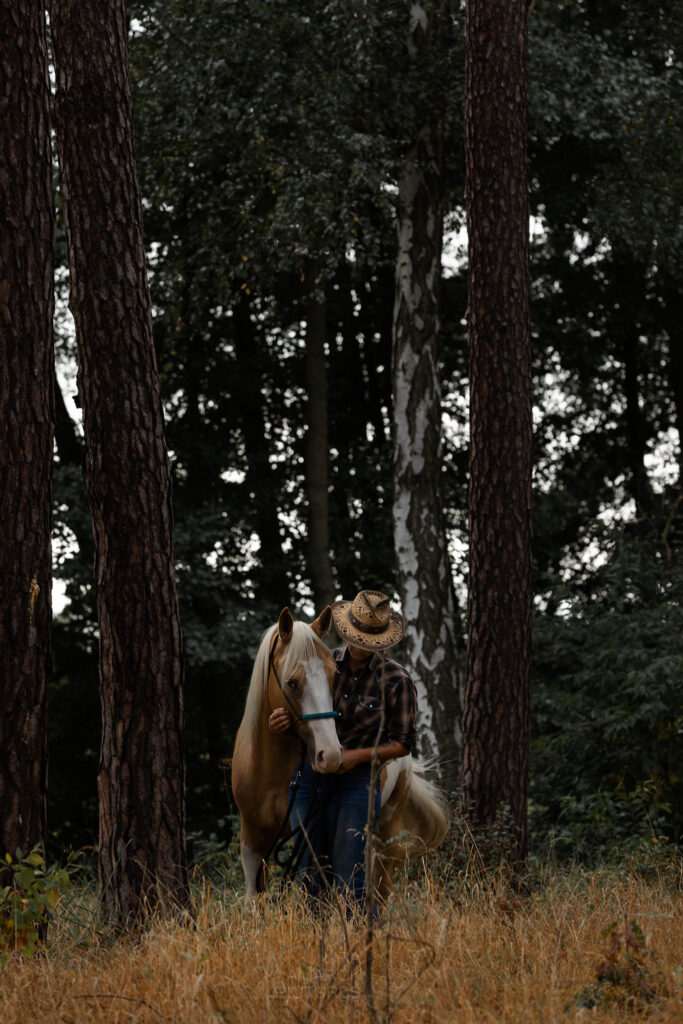 Frau und Pferd stehen dicht beisammen und kuscheln im Wald