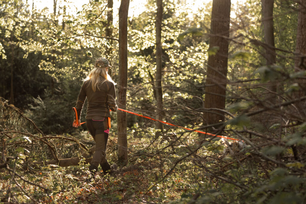 Jägerin geht mit ihrem Hund durch einen dicht bewachsenen Wald bei der Nachsuche