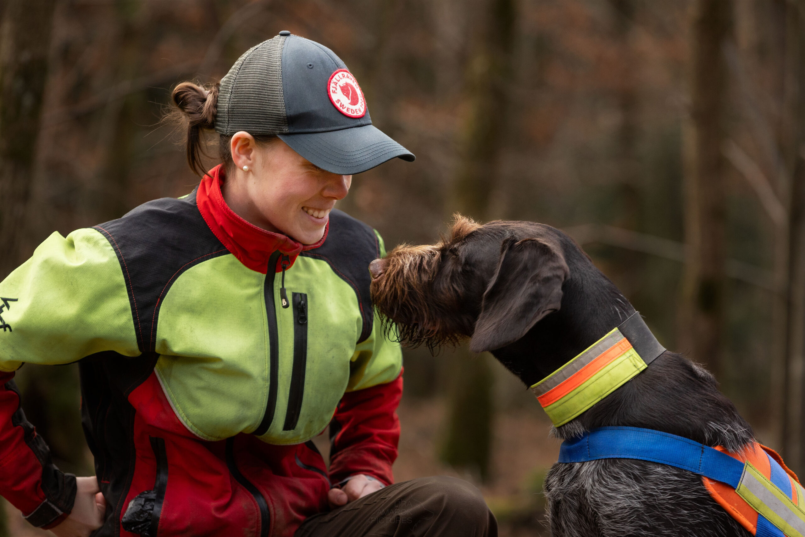 Ein Deutsch Drahthaar und eine Frau schauen sich an, die Frau lächelt. Beide tragen Signalkleidung