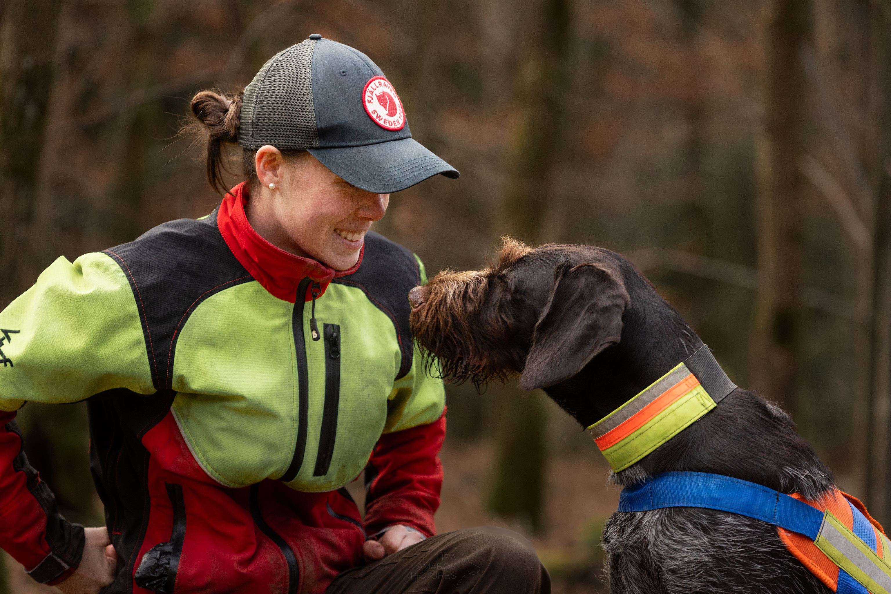 Ein Deutsch Drahthaar und eine Frau schauen sich an, die Frau lächelt. Beide tragen Signalkleidung