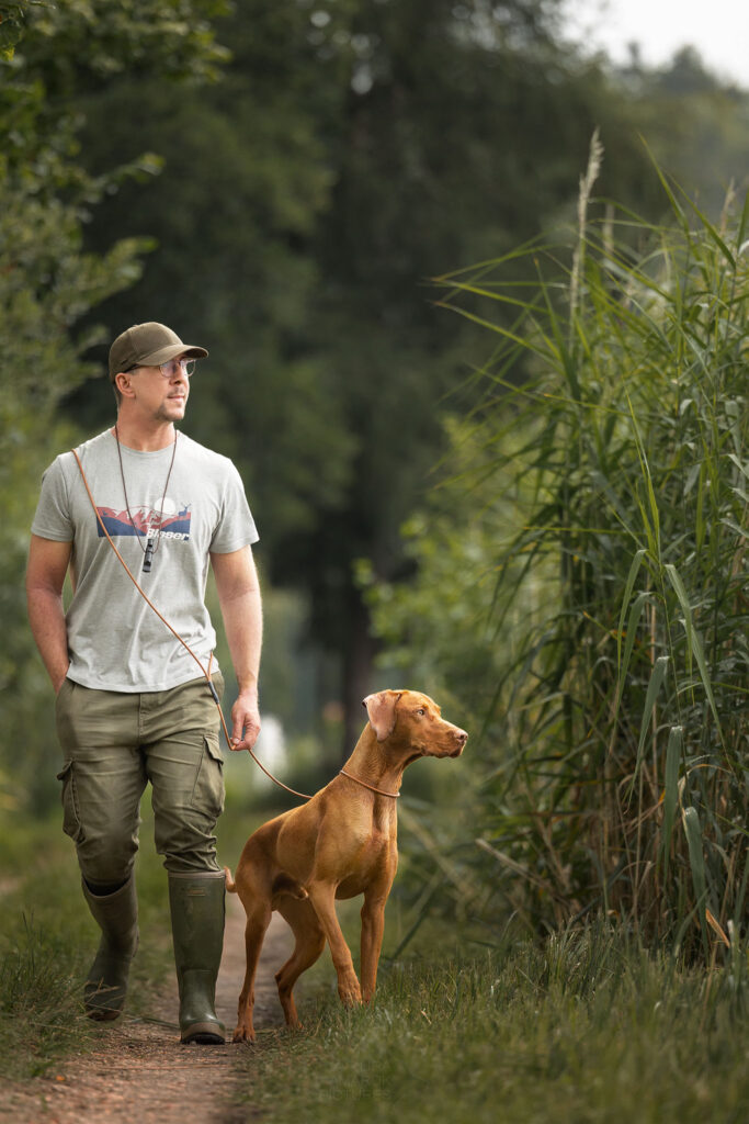 Ein Mann mit seinem Hund an der Pirschleine am Wasser