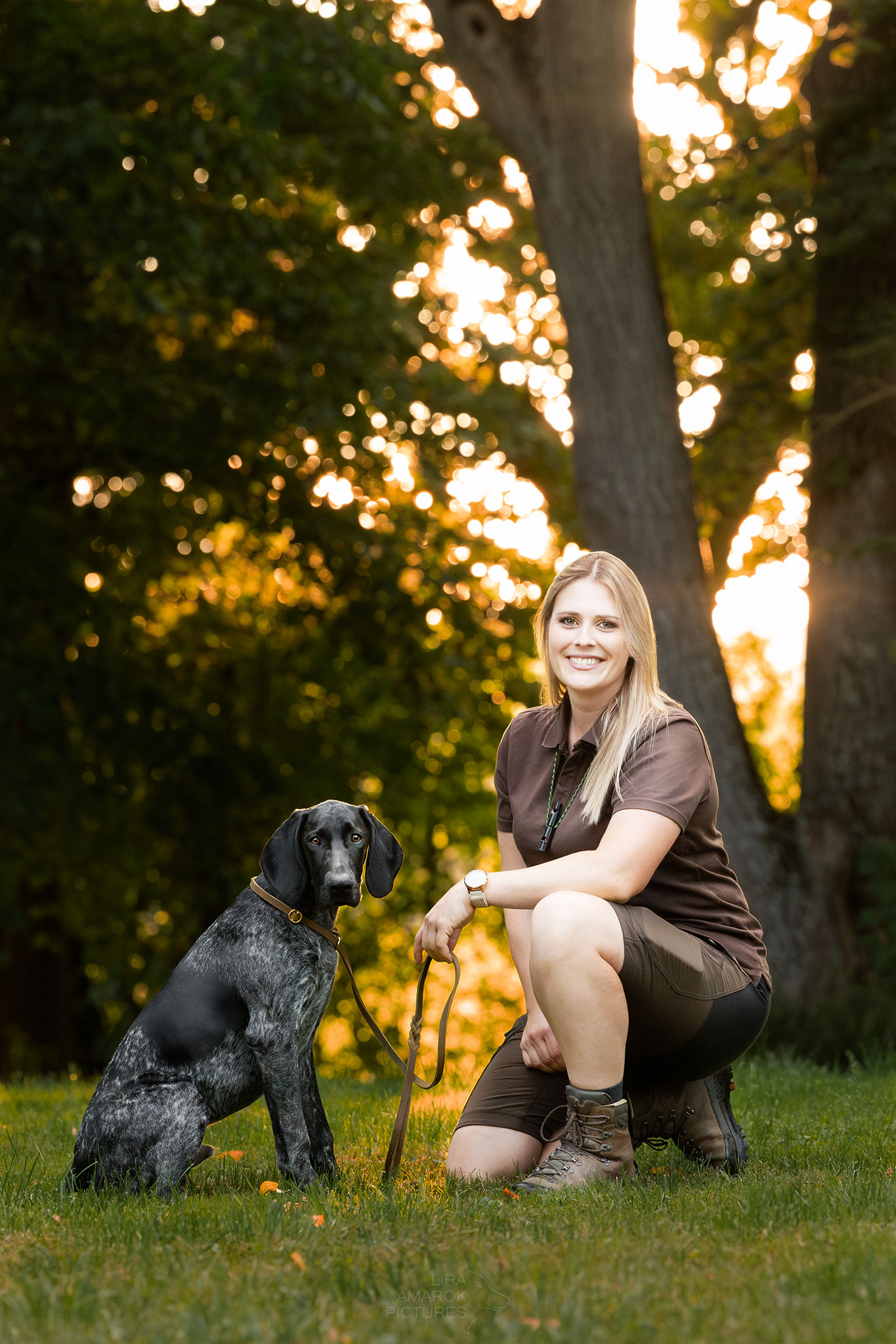 Eine Hundeführerin sitzt mit ihrem jungen Jagdhund im Sonnenuntergang