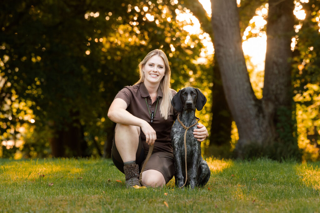 Ein Team von Hundeführerin und Jagdhund sitzen gemeinsam im Sonnenuntergang