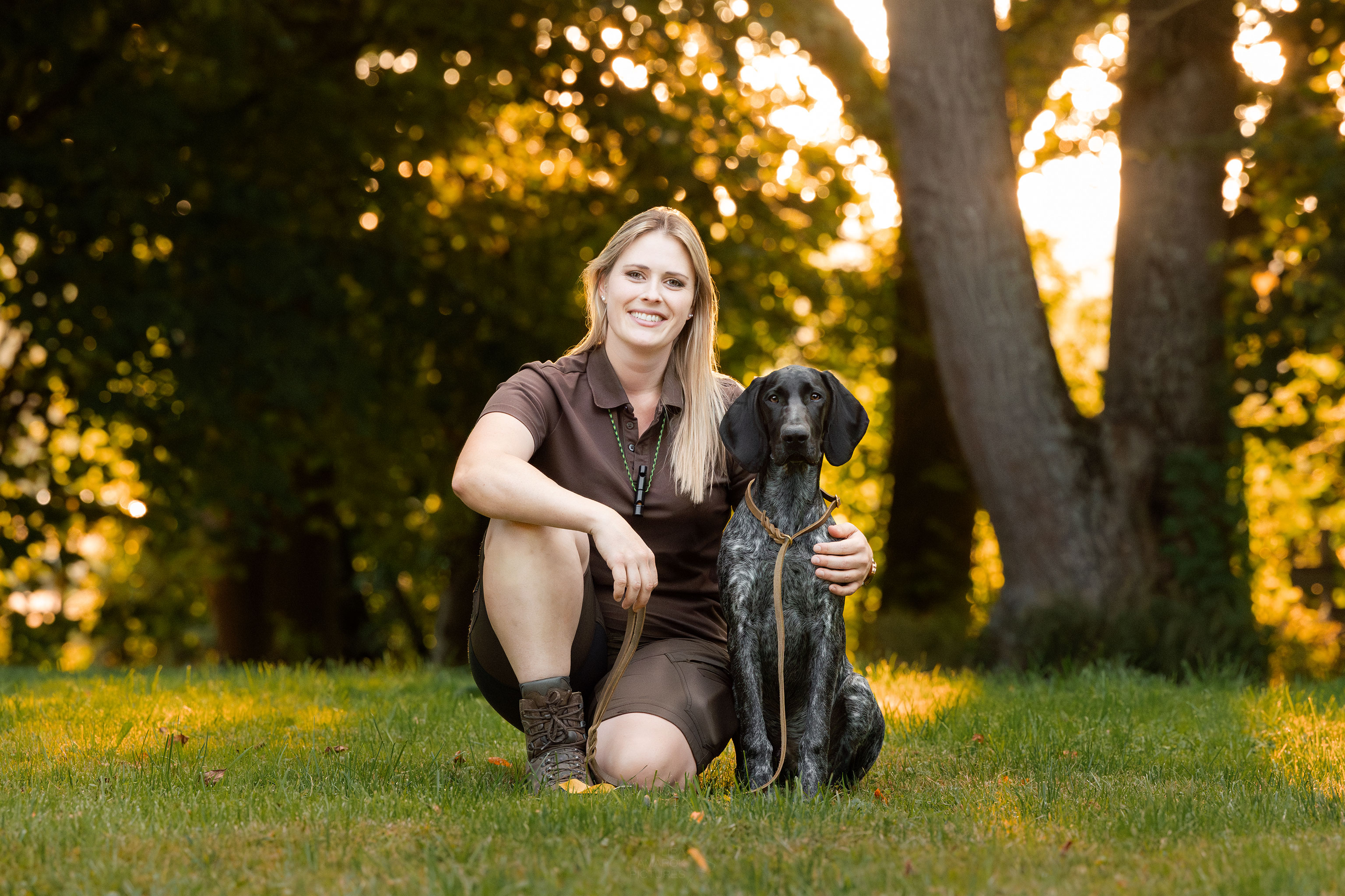 Ein Team von Hundeführerin und Jagdhund sitzen gemeinsam im Sonnenuntergang
