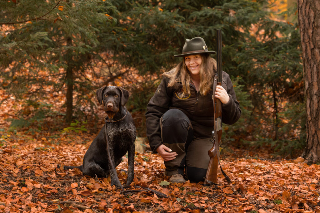 Eine Jägerin mit Flinte und ihrem Deutsch Drahthaar an ihrer Seite