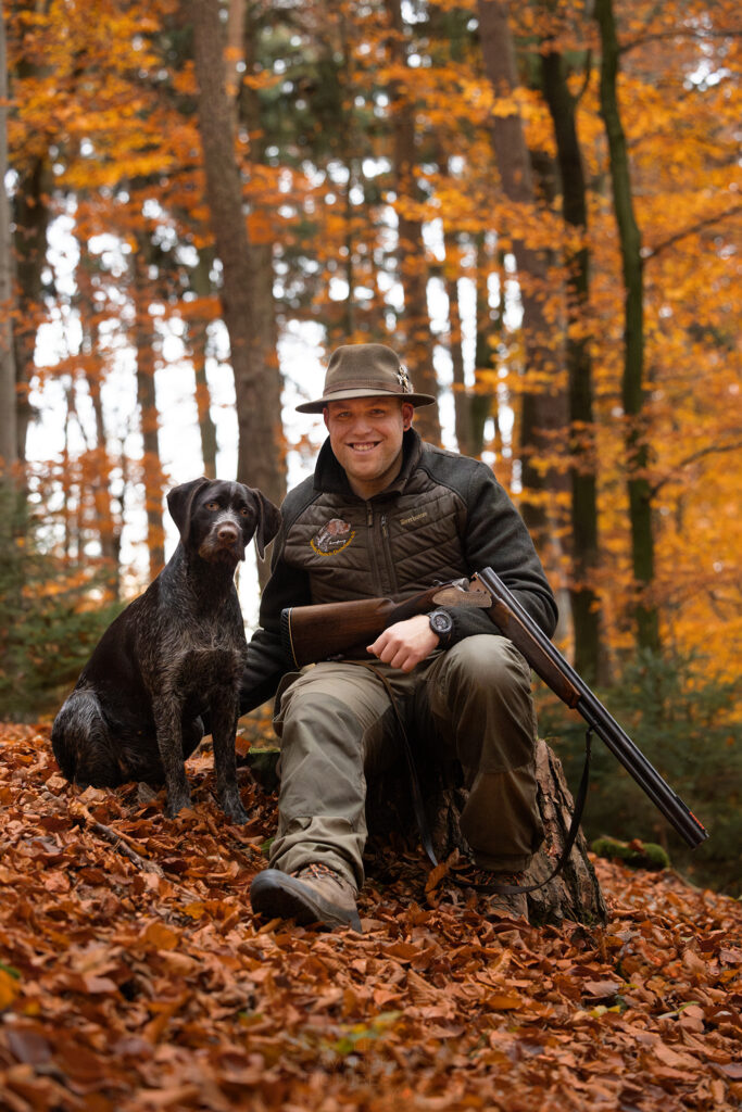 Ein Jäger sitzt im Wald mit seiner gebrochenen Flinte und seinem Jagdhund an seiner Seite